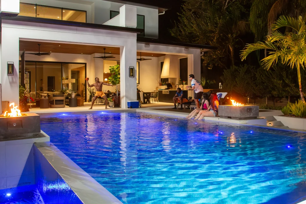 Friends enjoying a luxury pool with LED lighting, fire features, and a waterfall like infinity pool feature in Orlando.